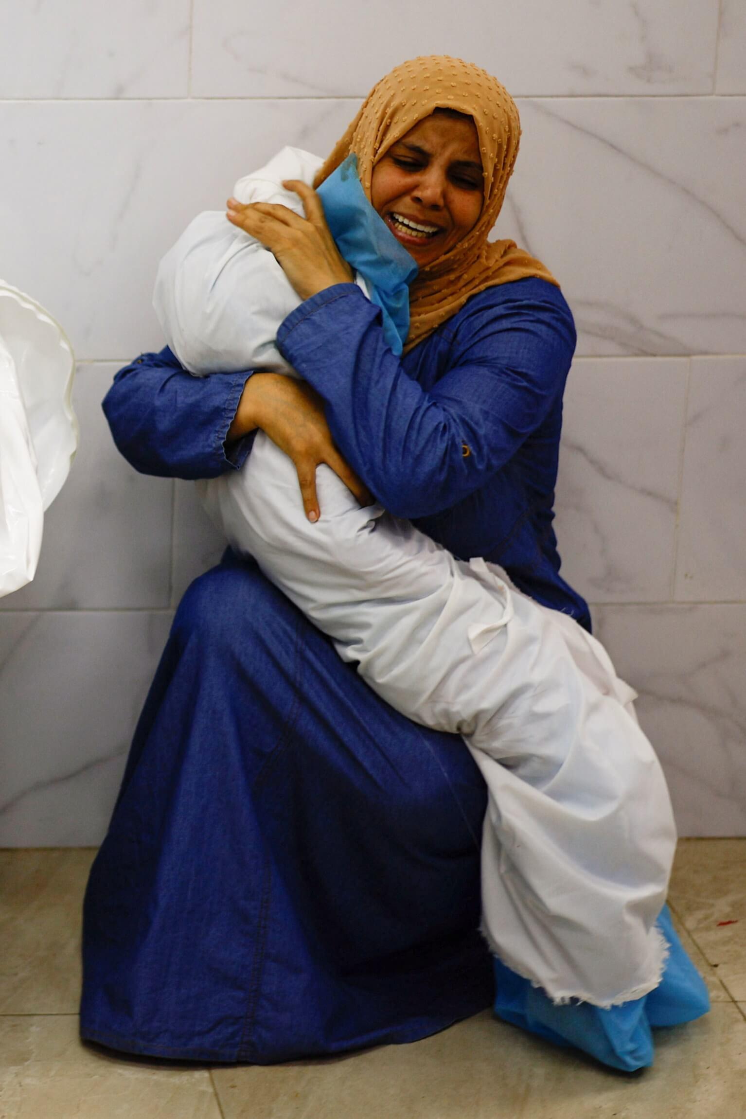 A Palestinian woman showing her face holds the body of her dead niece