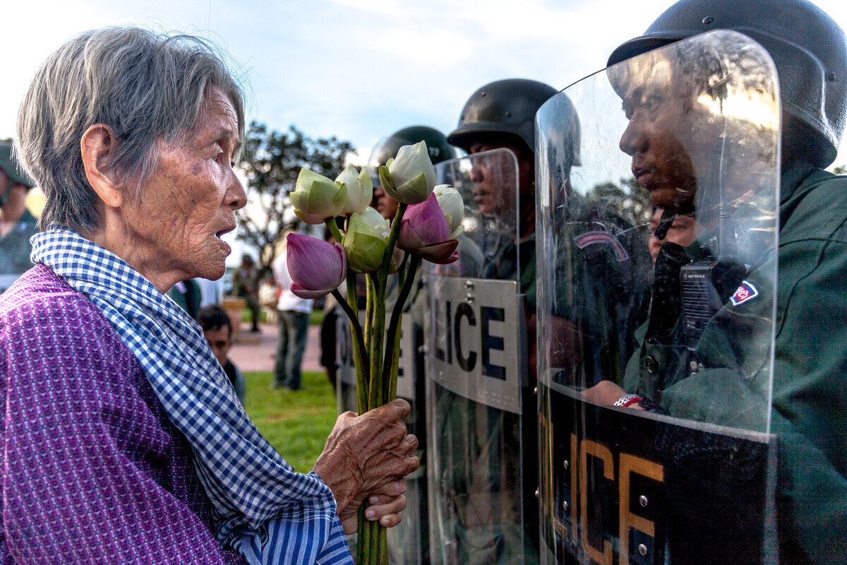 PHNOM PENH, CAMBODIA - September 06: Boeung Kak Lake activist Nget Khun offers lotus flowers to police forces gathered to impede a demonstration by different activist groups in front of the Ministry of Defence in Phnom Penh, Cambodia on September 06, 2013. Since Boeung Kak Lake was leased to a private company in 2007, resulting in the evictions of surrounding communities in 2009, a group of women from the Lake has taken the forefront of the fight for their rights. Although their activism was initially dedicated to saving their homes, they are now some of Cambodia's most well-known, outspoken and fearless activists, becoming an iconic symbol of the fight of human rights and justice in Cambodia. Photo by Omar Havana